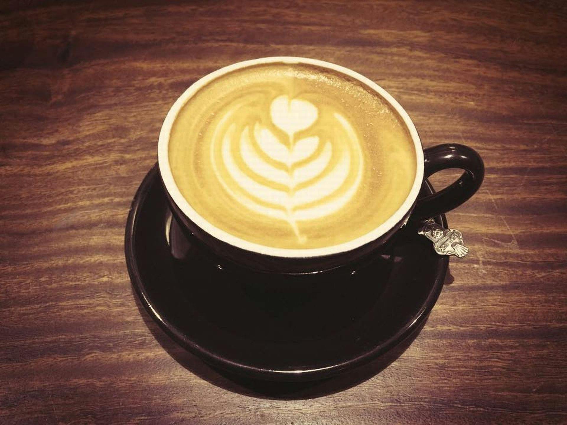 Elegant latte art in a cappuccino on a wooden table in a black cup and saucer.