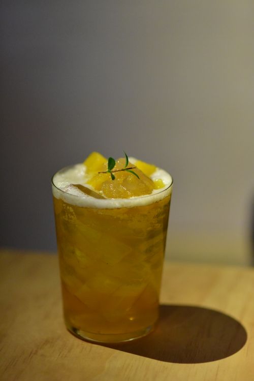 Free Closeup of a cool citrus cocktail in a tall glass with ice, foam, and herb garnish on a wooden table. Stock Photo