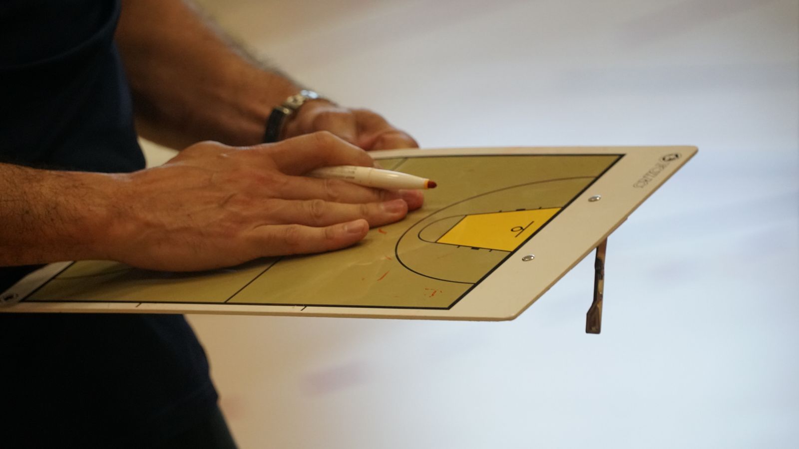 Close de uma prancheta tática de basquete sendo usada por um técnico para desenhar jogadas