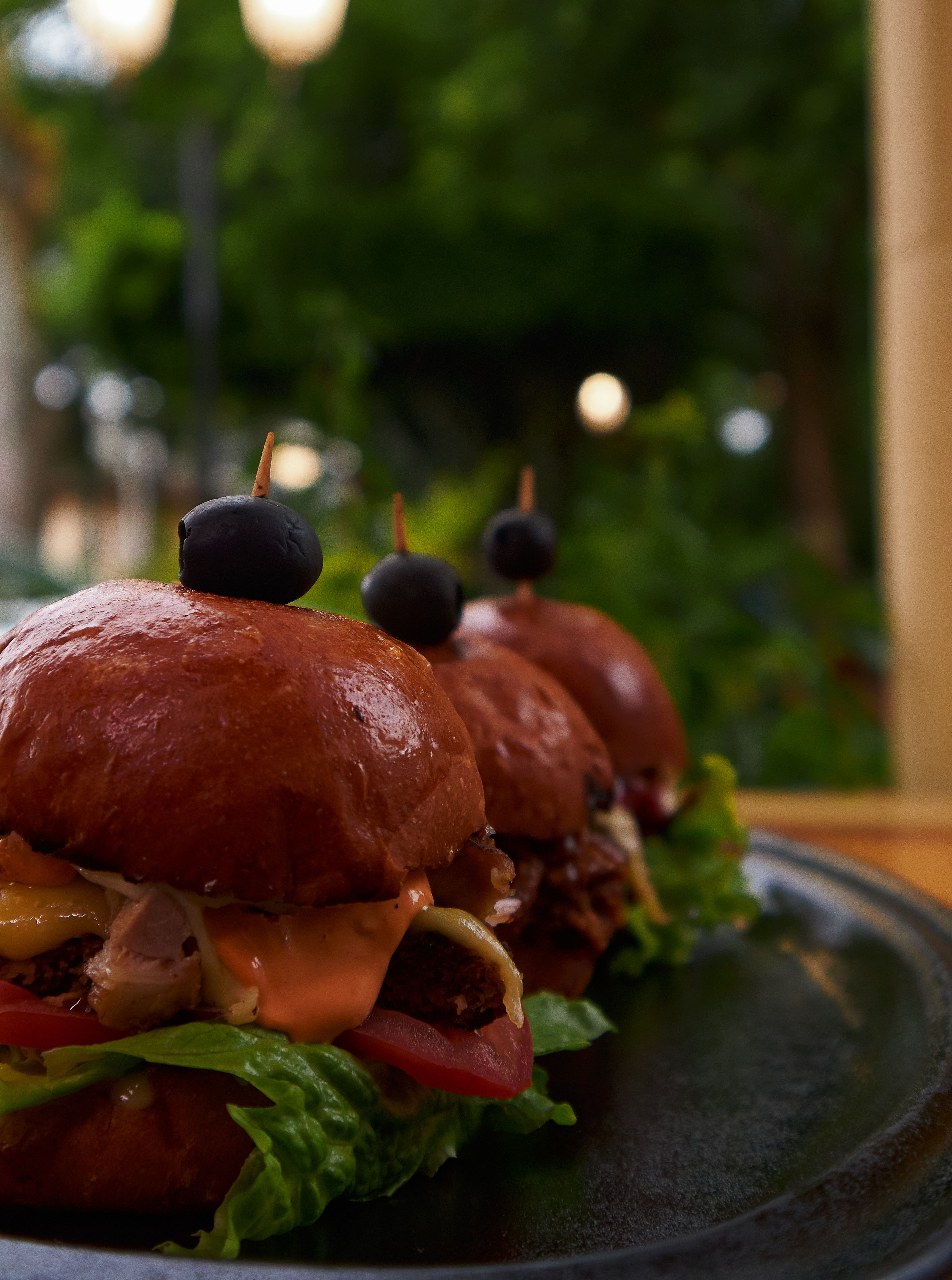Delicious gourmet sliders with olives served on a black plate outdoors. Perfect for food lovers.