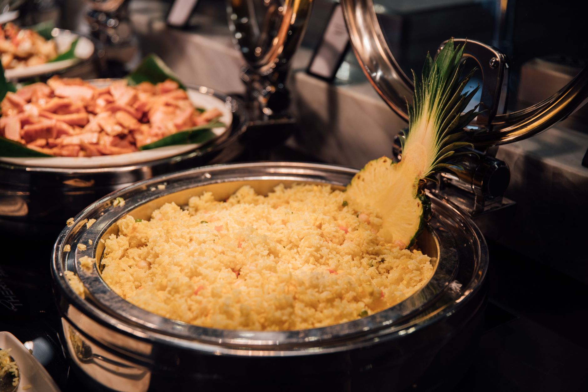 A buffet serving of yellow fried rice garnished with pineapple slice, highlighting tropical flavors.