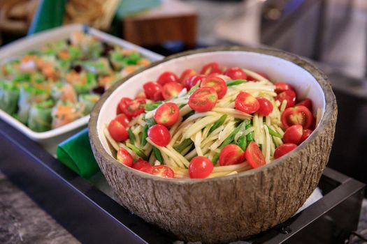 A vibrant papaya salad with cherry tomatoes in a coconut bowl, perfect for Thai cuisine lovers.