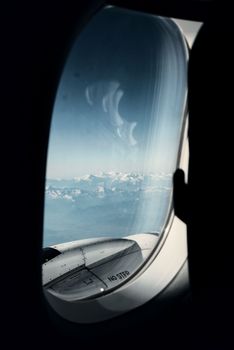A high-altitude view of snowy mountains visible through an airplane window.