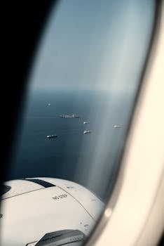 Aerial view of cargo ships in the ocean from an airplane window, showcasing global trade.