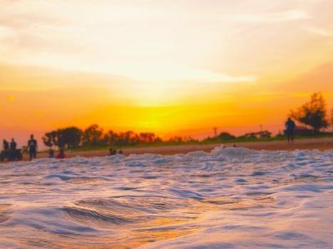 A serene beach at sunset with gentle waves and silhouettes of people, captured in warm colors.