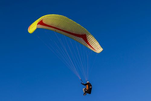 Free Experience the thrill of paragliding against a flawless blue sky, capturing freedom and adventure in this dynamic aerial view. Stock Photo