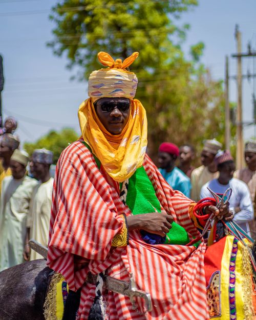 Free Man in traditional African attire riding horse during cultural parade. Stock Photo