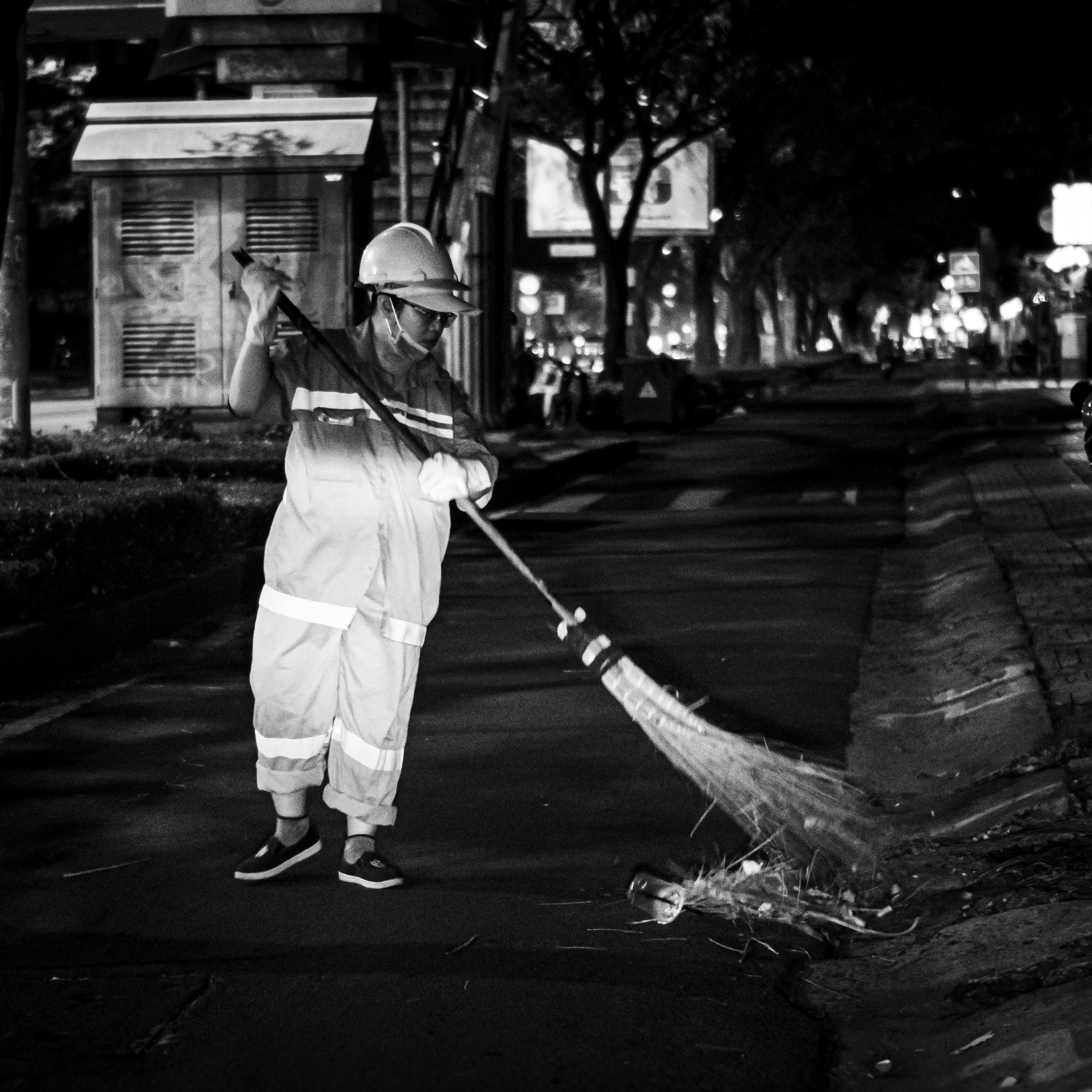 Black and white image of a street sweeper cleaning a city sidewalk at night.