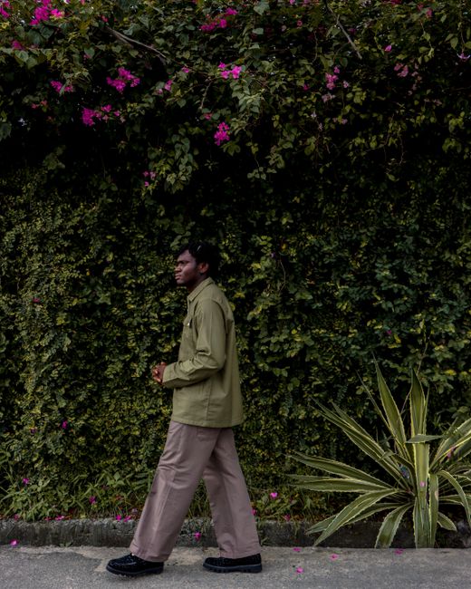 An adult man walks by a lush, flowering wall in a vibrant street scene.