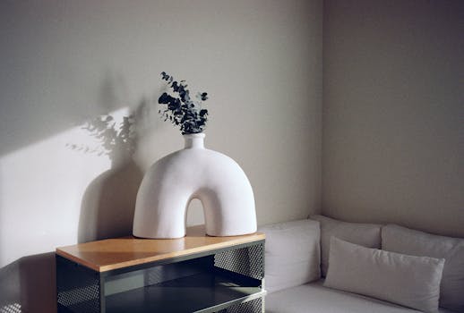 A cozy corner with a modern couch and a unique white ceramic vase on a wooden table.