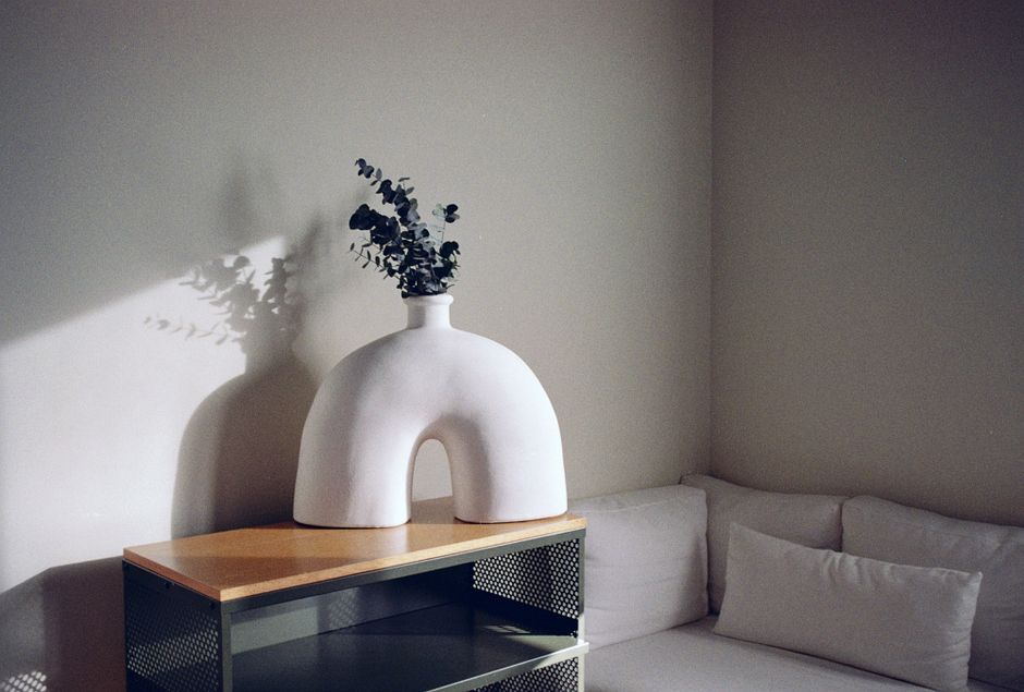 A cozy corner with a modern couch and a unique white ceramic vase on a wooden table.