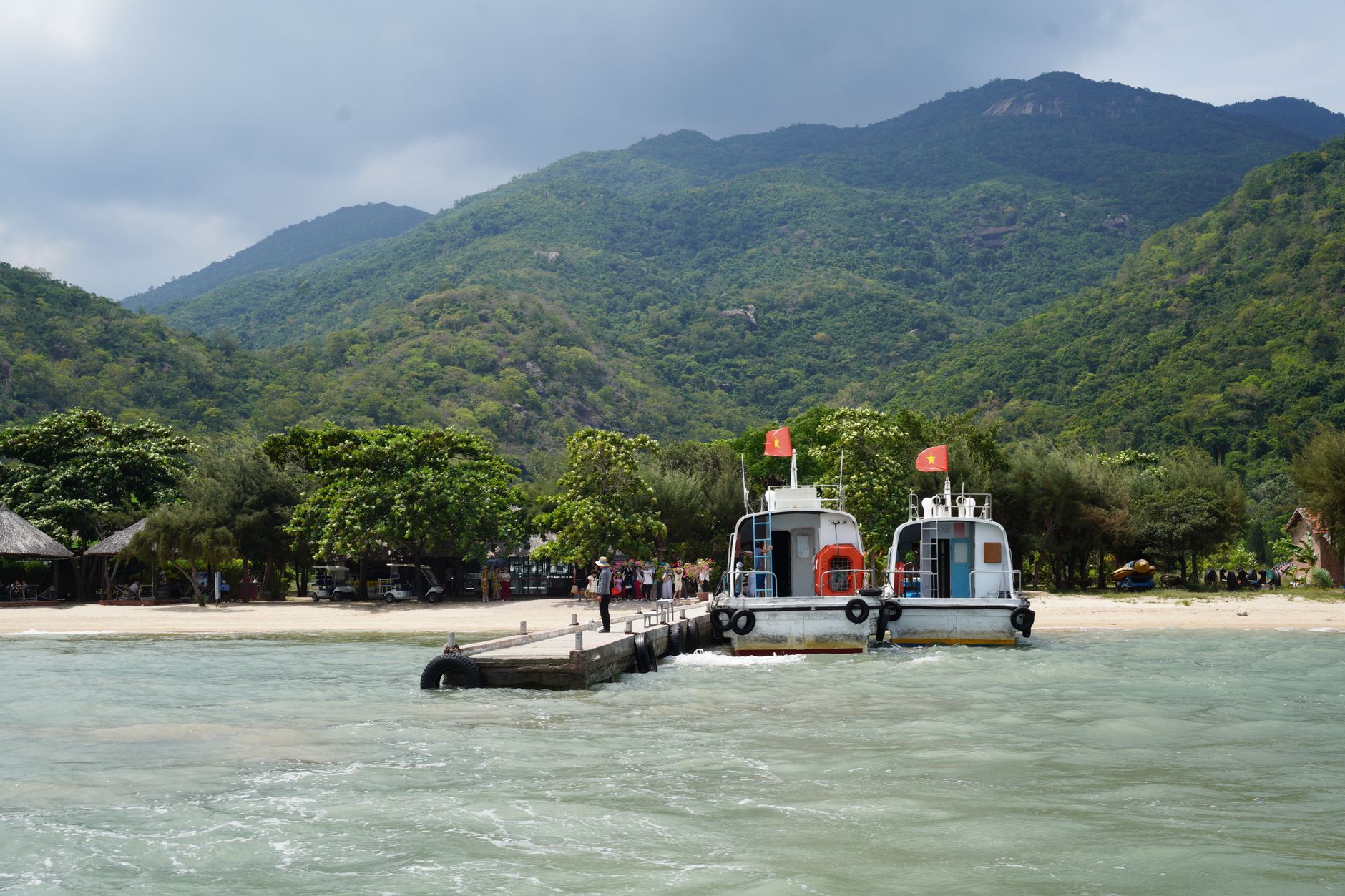A tranquil beach with boats docked and lush green mountains in the background.