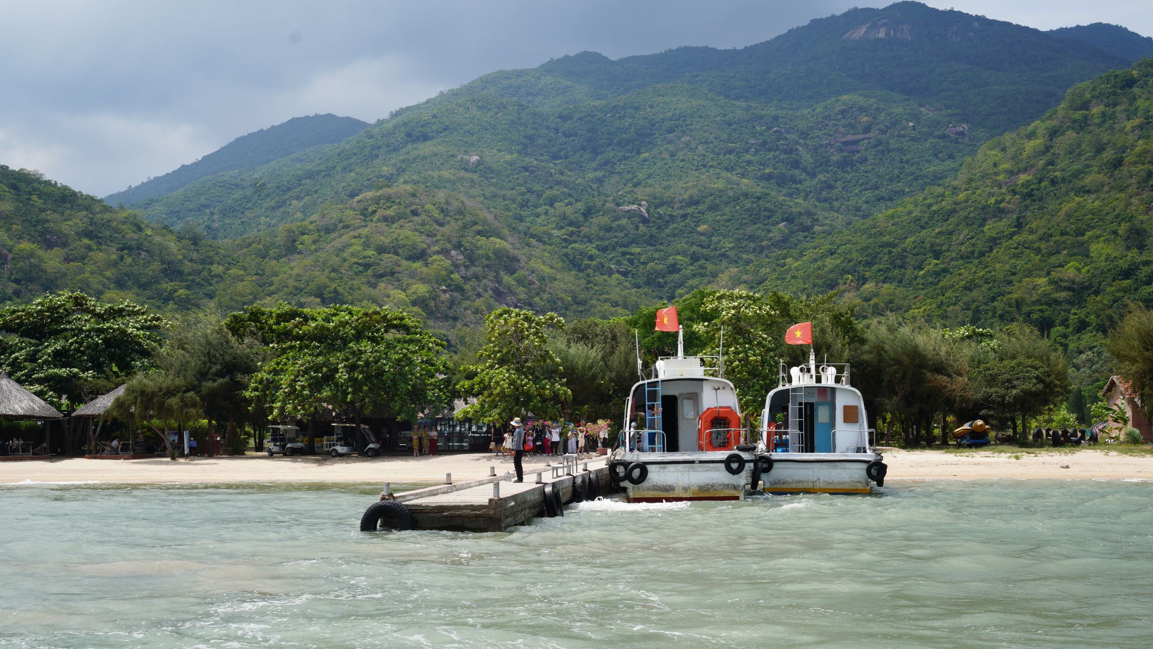 A tranquil beach with boats docked and lush green mountains in the background.