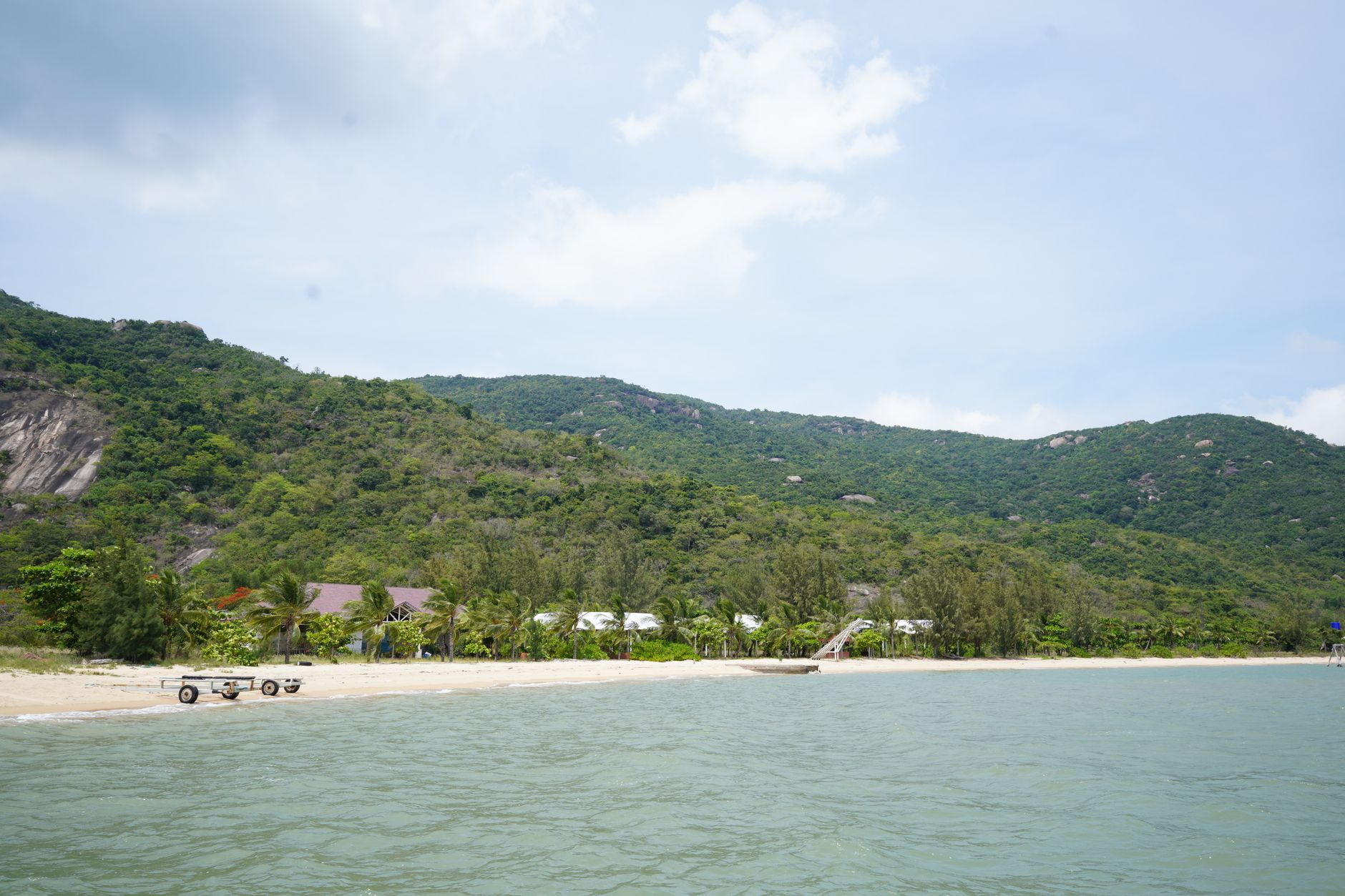Serene beach with lush green hills under a bright sky, capturing tranquility.