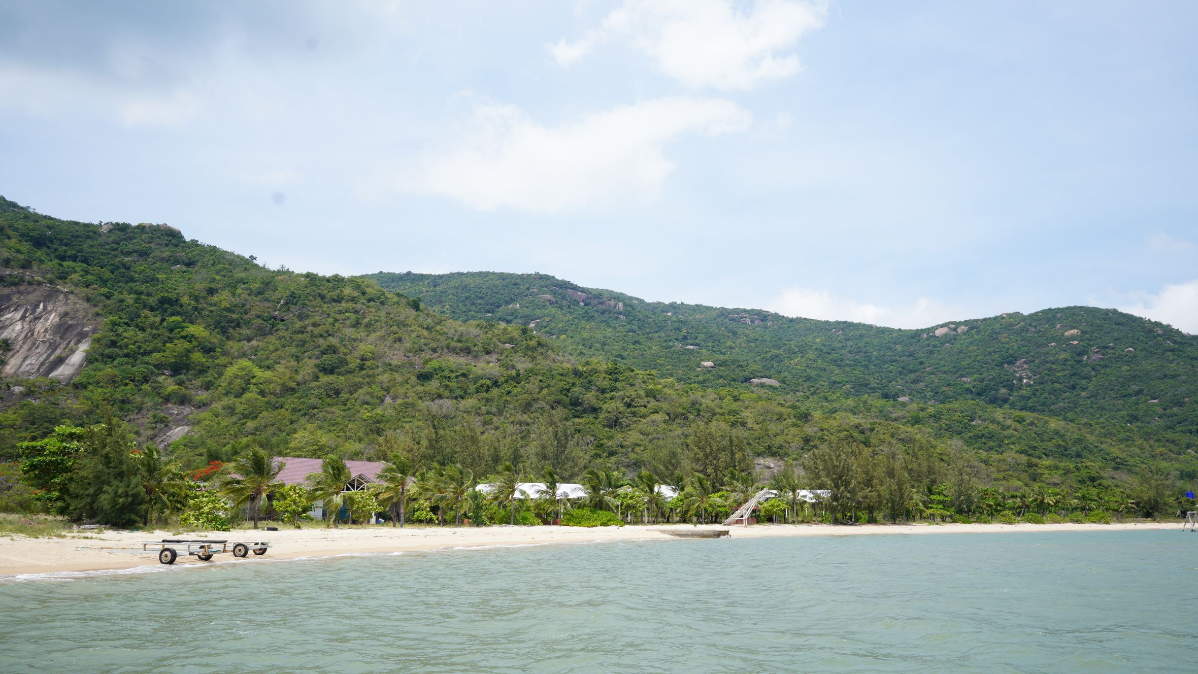 Serene beach with lush green hills under a bright sky, capturing tranquility.