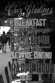 Black and white photo capturing reflective French cafe signage in Paris. People walking by.