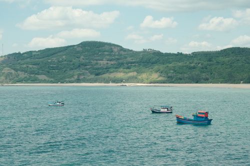 Free Three colorful boats float on tranquil waters near green hills under a blue sky. Stock Photo