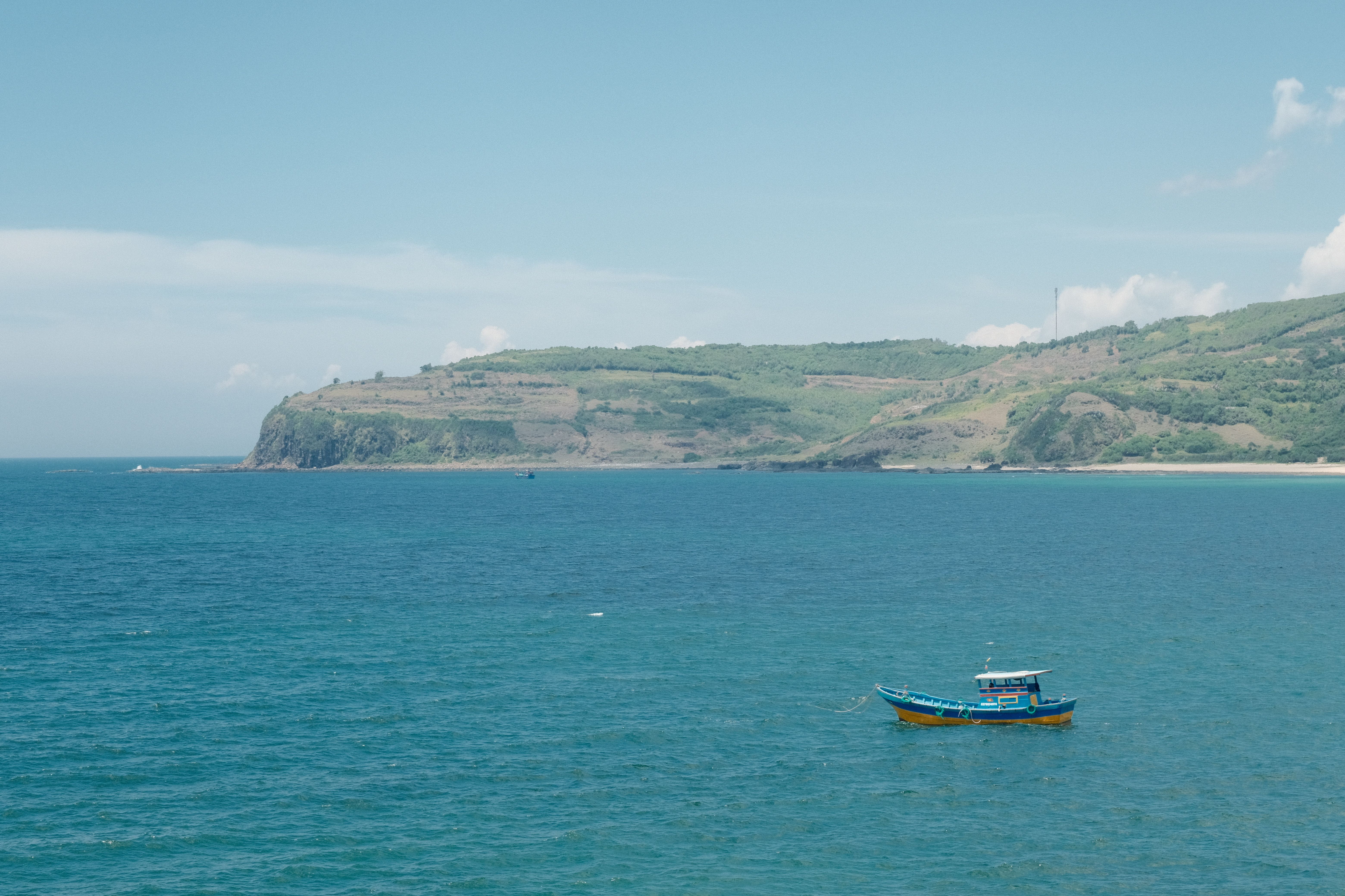 A serene view of a blue boat floating on expansive ocean waters near a lush green coastline.