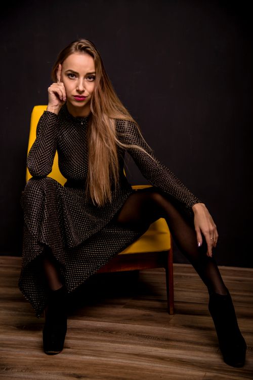 Free Sophisticated woman in polka dot dress sitting on a yellow chair in a dark room looking confident. Stock Photo