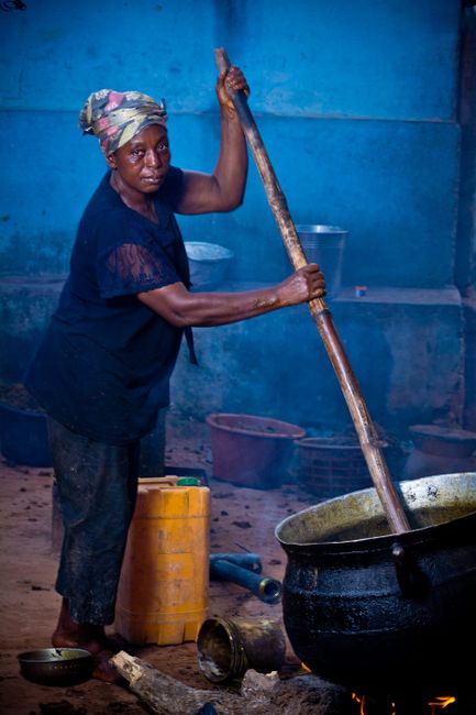 Elderly woman stirring a large pot outdoors in Ghana, showcasing traditional cooking.