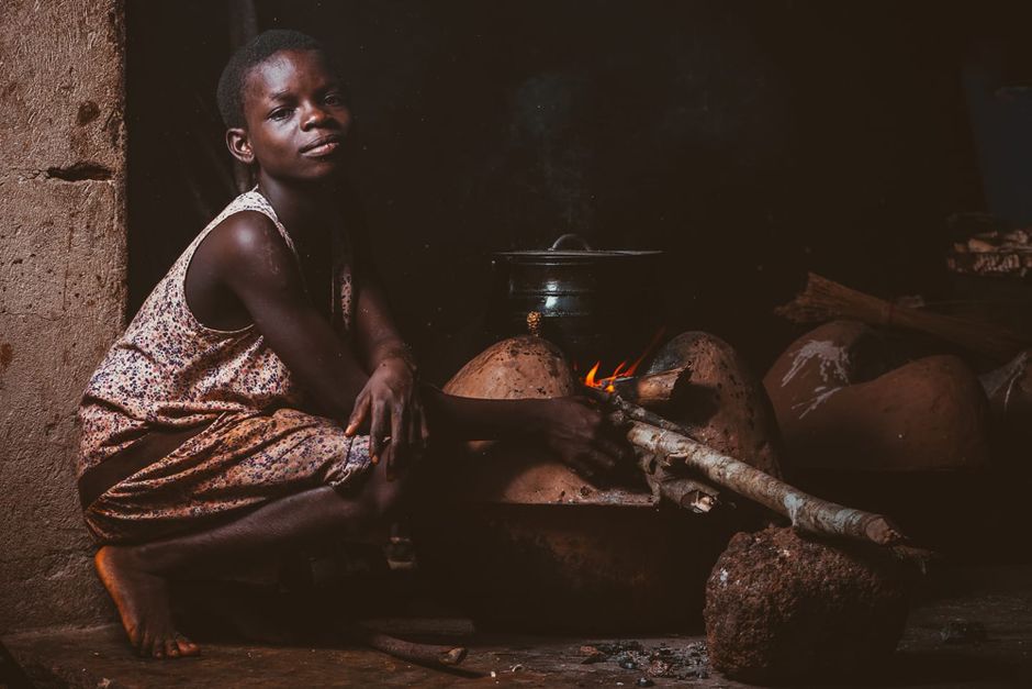 A child prepares a meal using a traditional oven in a village setting in Ghana.