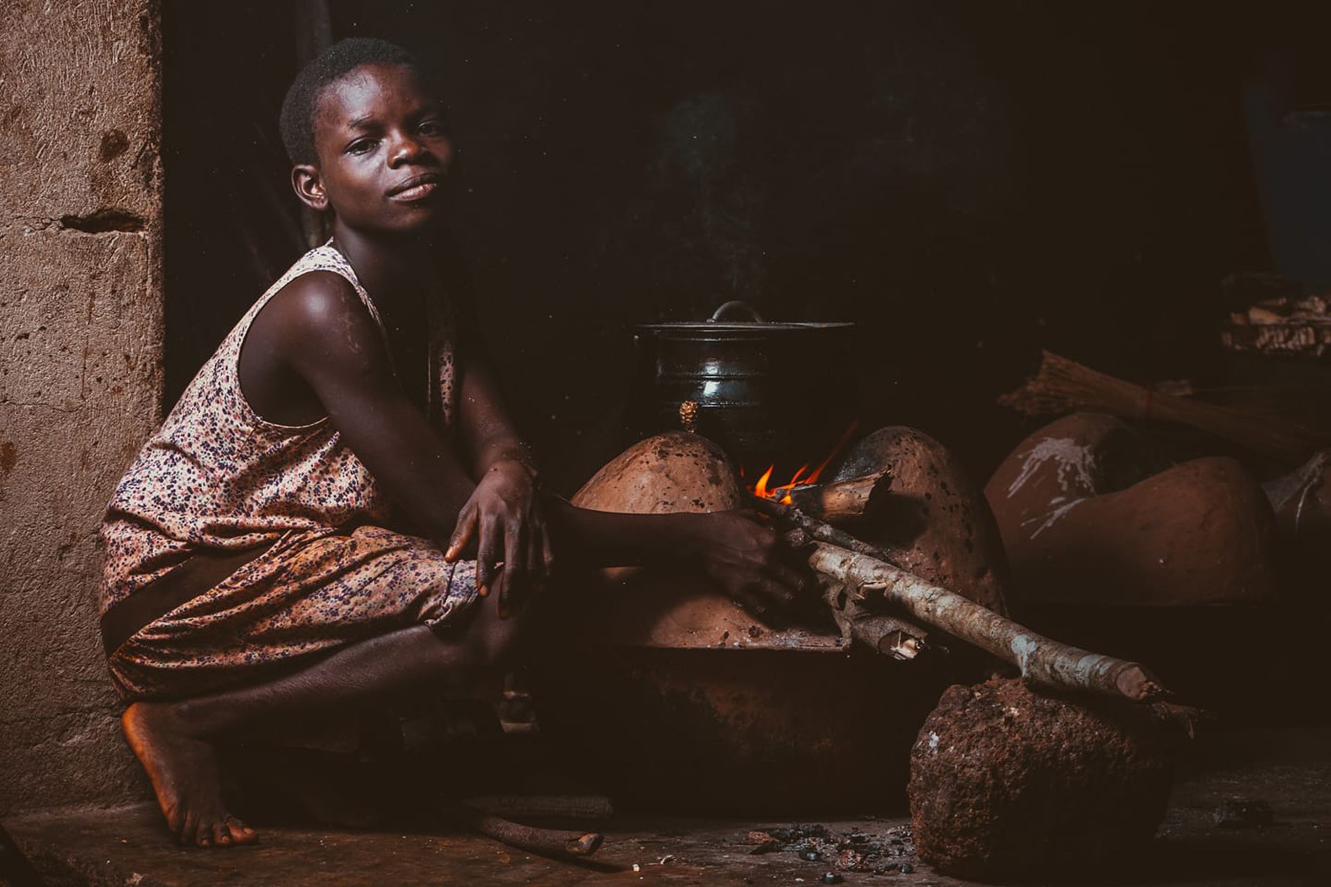 A child prepares a meal using a traditional oven in a village setting in Ghana.