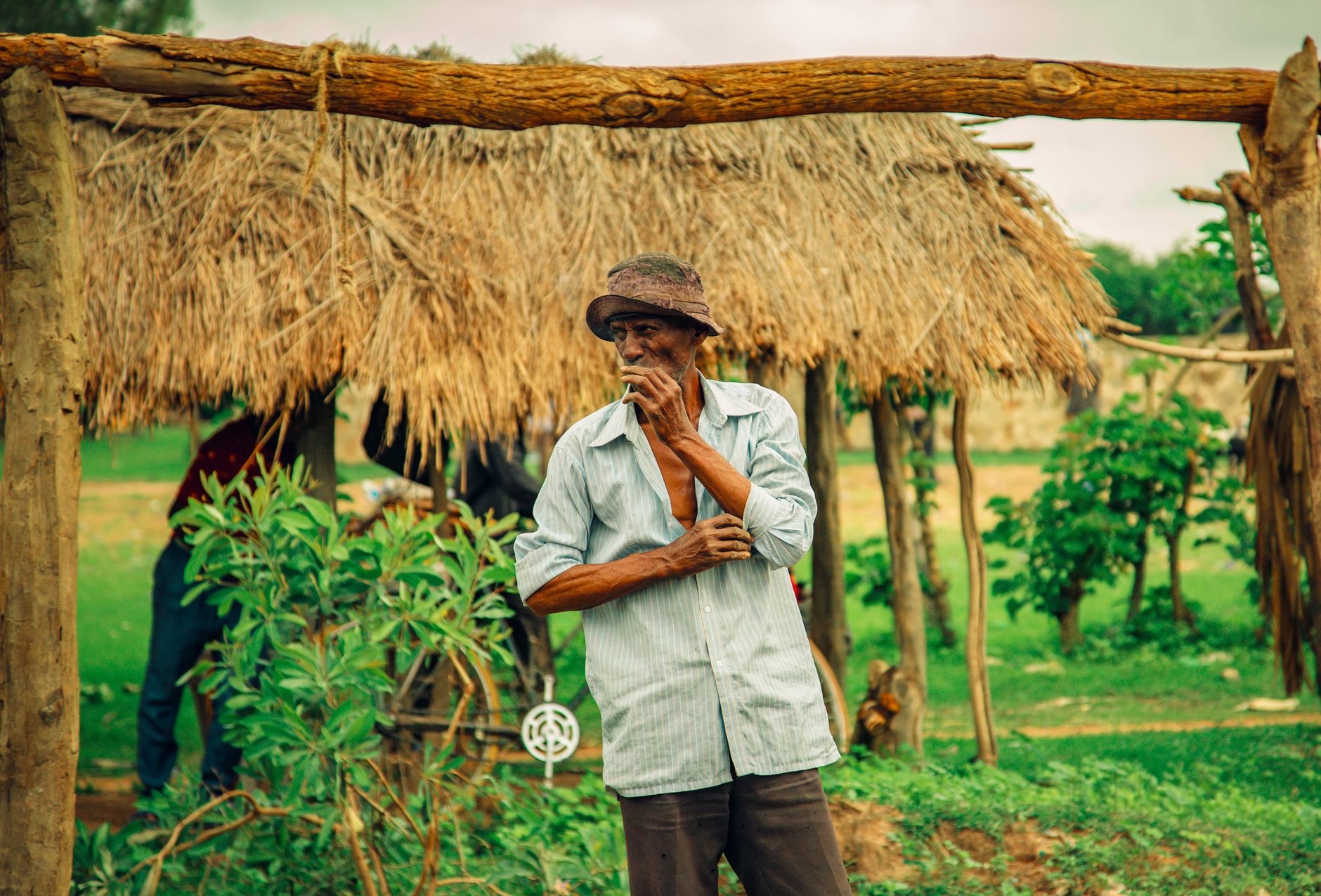 A Tanzanian farmer stands pensively under a thatched roof in a rural setting, embodying traditional life.
