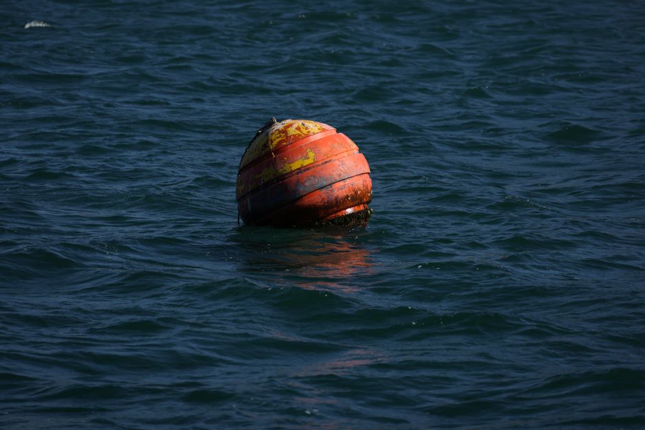 Photograph of a red buoy bobbing on the ocean surface during daytime, capturing nautical themes.