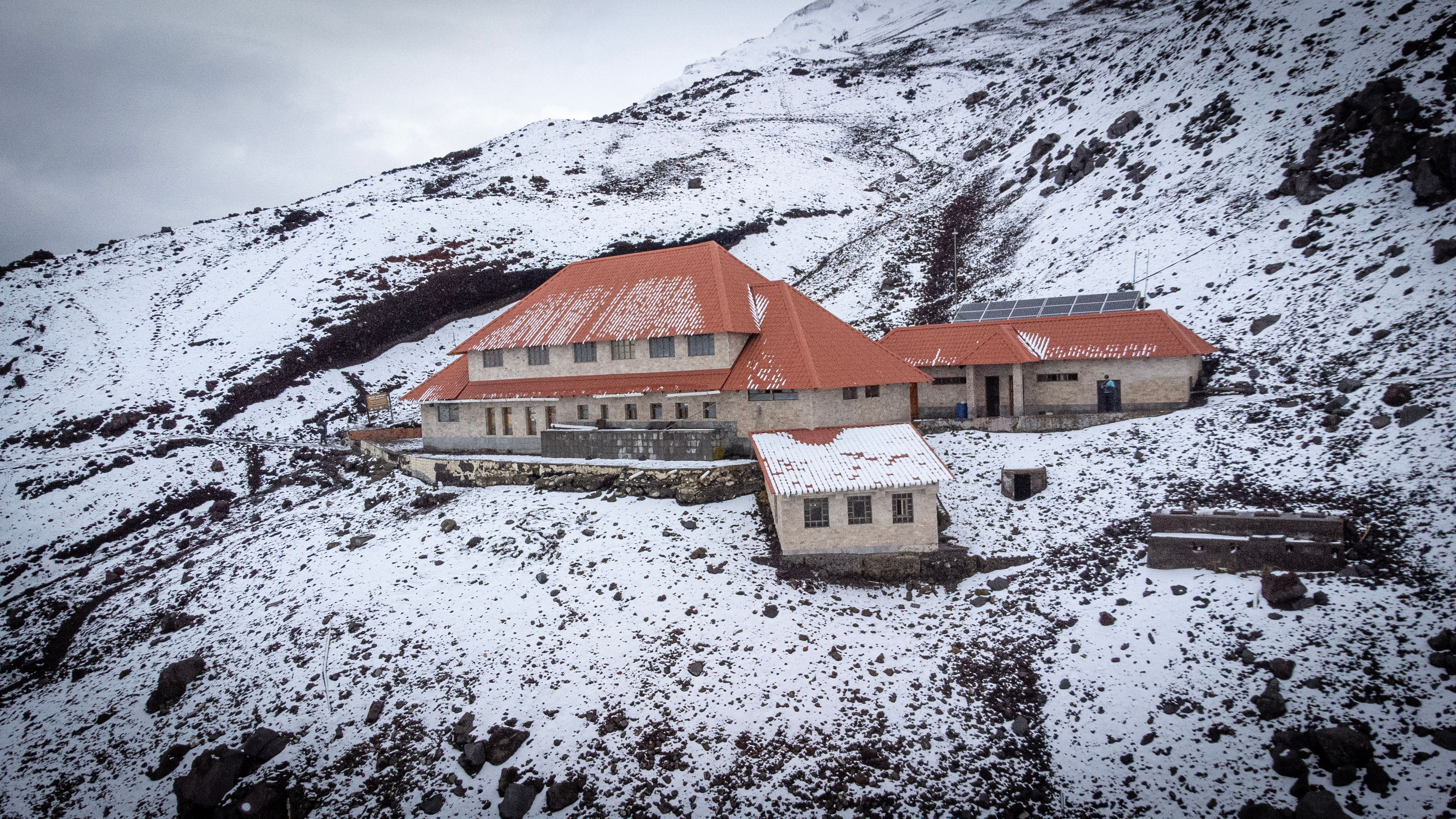 A lodge with red roofs sits on the snowy slopes of Cotopaxi Volcano in Ecuador.