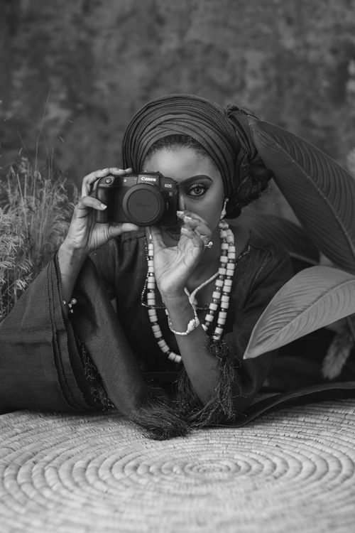 Free Black and white portrait of a woman with a camera, wearing traditional beads and headwrap. Stock Photo