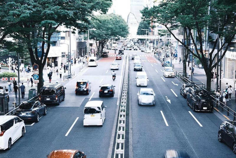 Scène dynamique d'une rue animée de Tokyo avec circulation et piétons sous des arbres verts