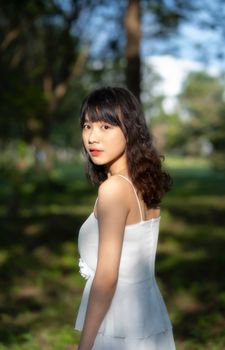 一位美丽的女子身着白色连衣裙，在宁静的户外环境中，自然光衬托出她的优雅