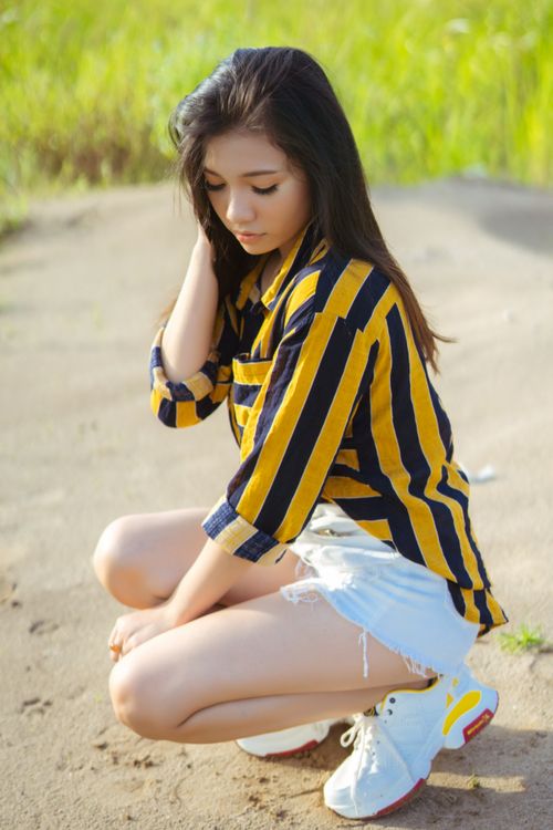 Free A young woman in a striped shirt poses outdoors in the sun. Stock Photo