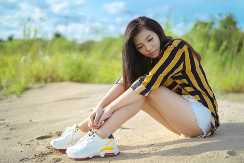 Free A young woman in a striped shirt and shorts enjoying a sunny day outdoors, sitting on sandy ground. Stock Photo