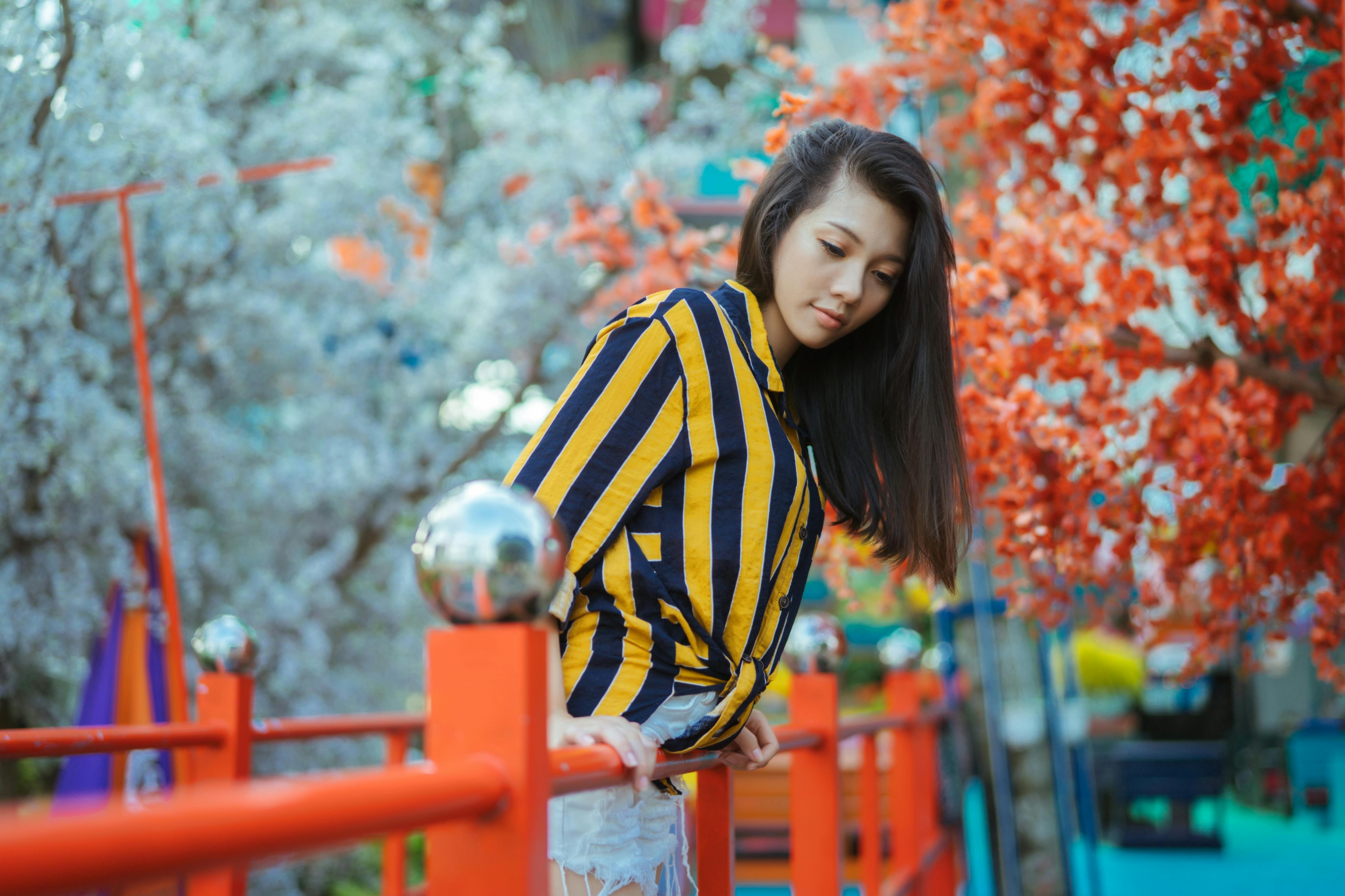 在时髦的条纹衣服的妇女倚靠在五颜六色的户外桥梁与开花的树.