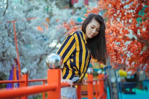 一位穿着时尚条纹服装的女人，倚靠在开满鲜花的树木下的五颜六色户外桥上