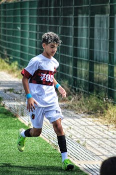 A young boy in a white soccer kit runs on a sunny outdoor field. Energetic youth sports scene.