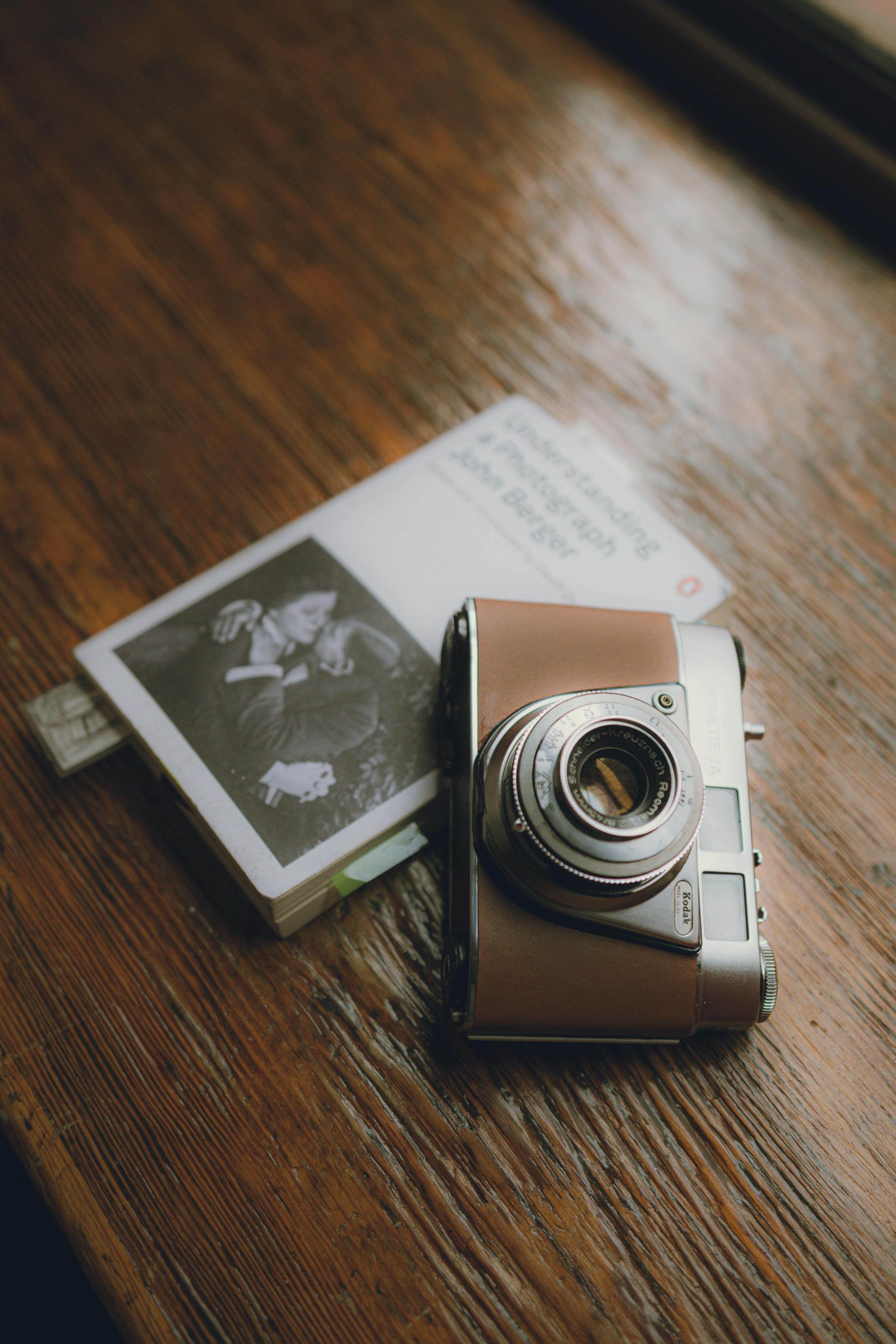 A vintage camera resting on a book atop a rustic wooden table, creating a nostalgic scene.