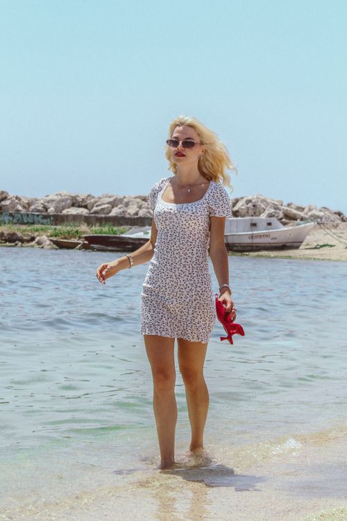 Free Blonde woman strolling on a sunny beach walk, relaxed summer vibe. Stock Photo