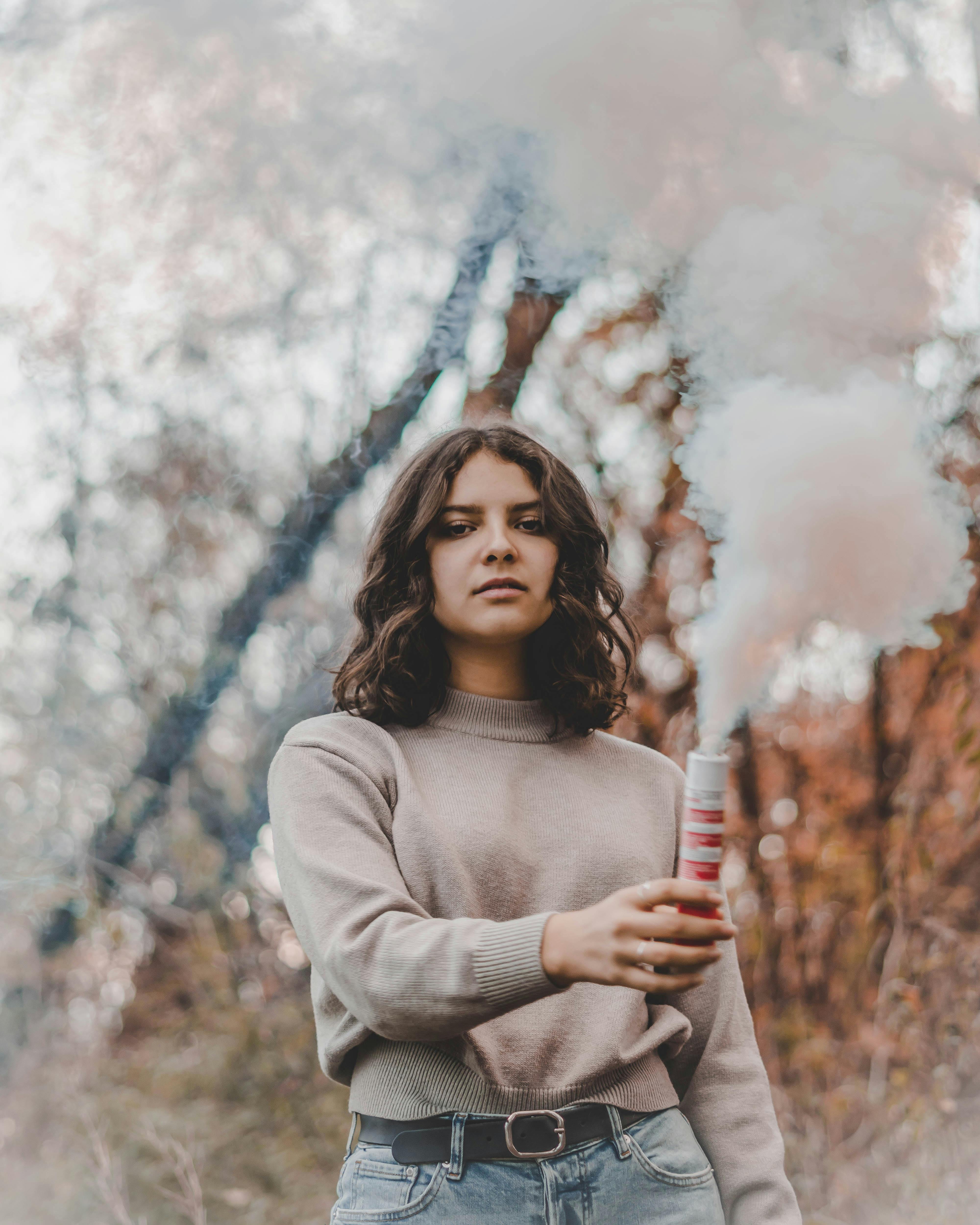 一位黑发女子手持烟雾弹立于秋叶之中，营造出戏剧性的照片效果