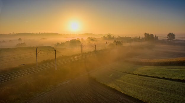 Captivating sunrise above misty fields with railway, creating a serene and magical ambiance.