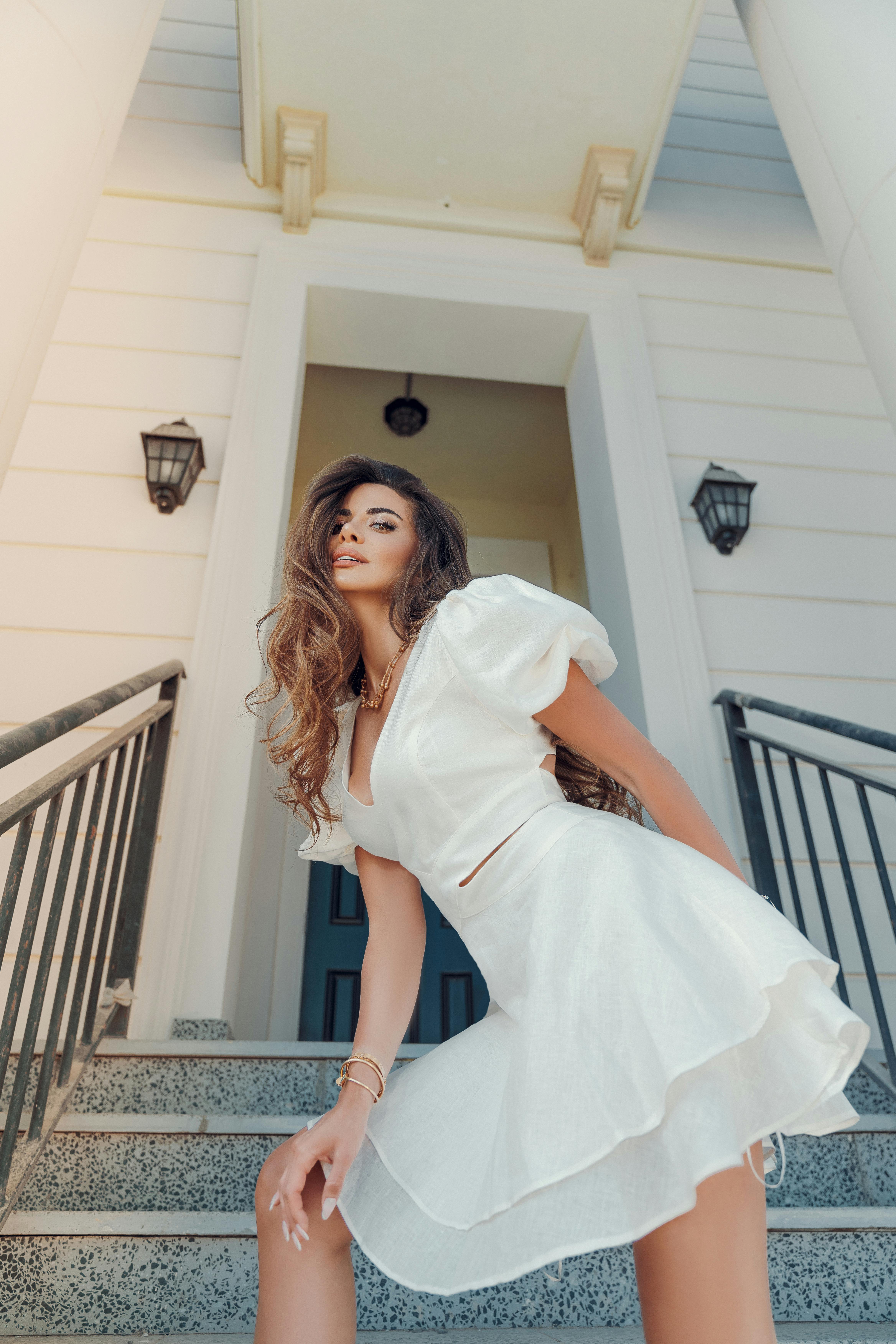 Free Fashionable woman in white dress posing on staircase outdoors, exuding elegance and confidence. Stock Photo