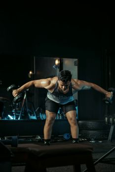 Focused athlete performing workout with dumbbells in dimly lit gym setting.