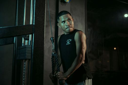 A dedicated man exercises with a cable machine in a gym, showcasing determination and strength.