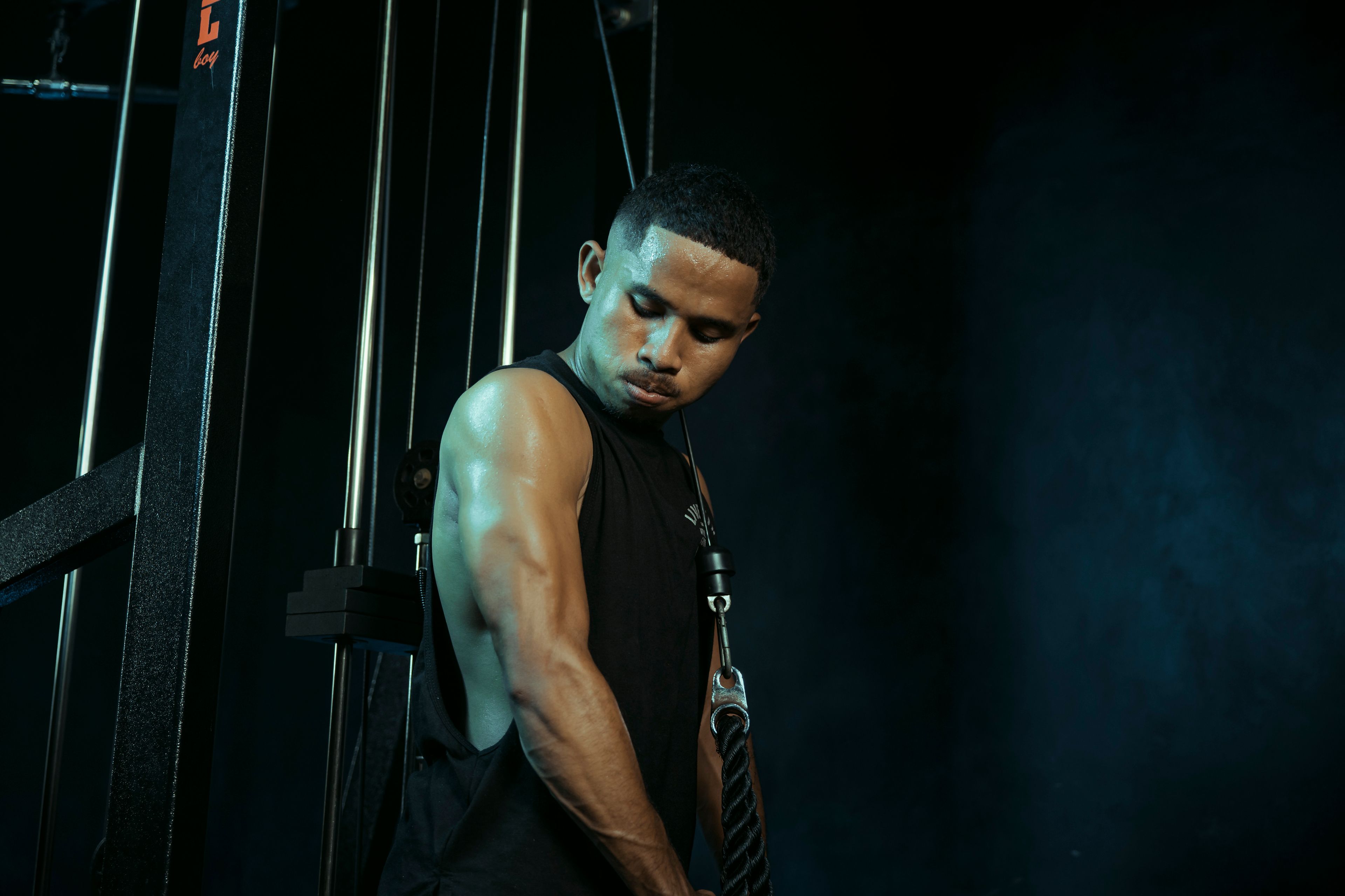 A man intensely exercising on a cable machine in a dark gym setting, highlighting fitness commitment.