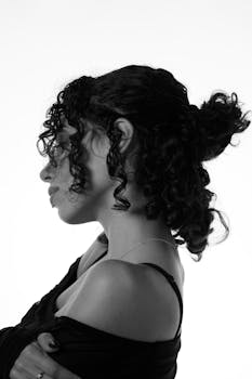Side profile of an elegant woman in black and white with curly hair and soft lighting.