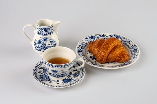 Free A croissant served with tea in a decorative porcelain set on a white backdrop, perfect for elegant tea time. Stock Photo