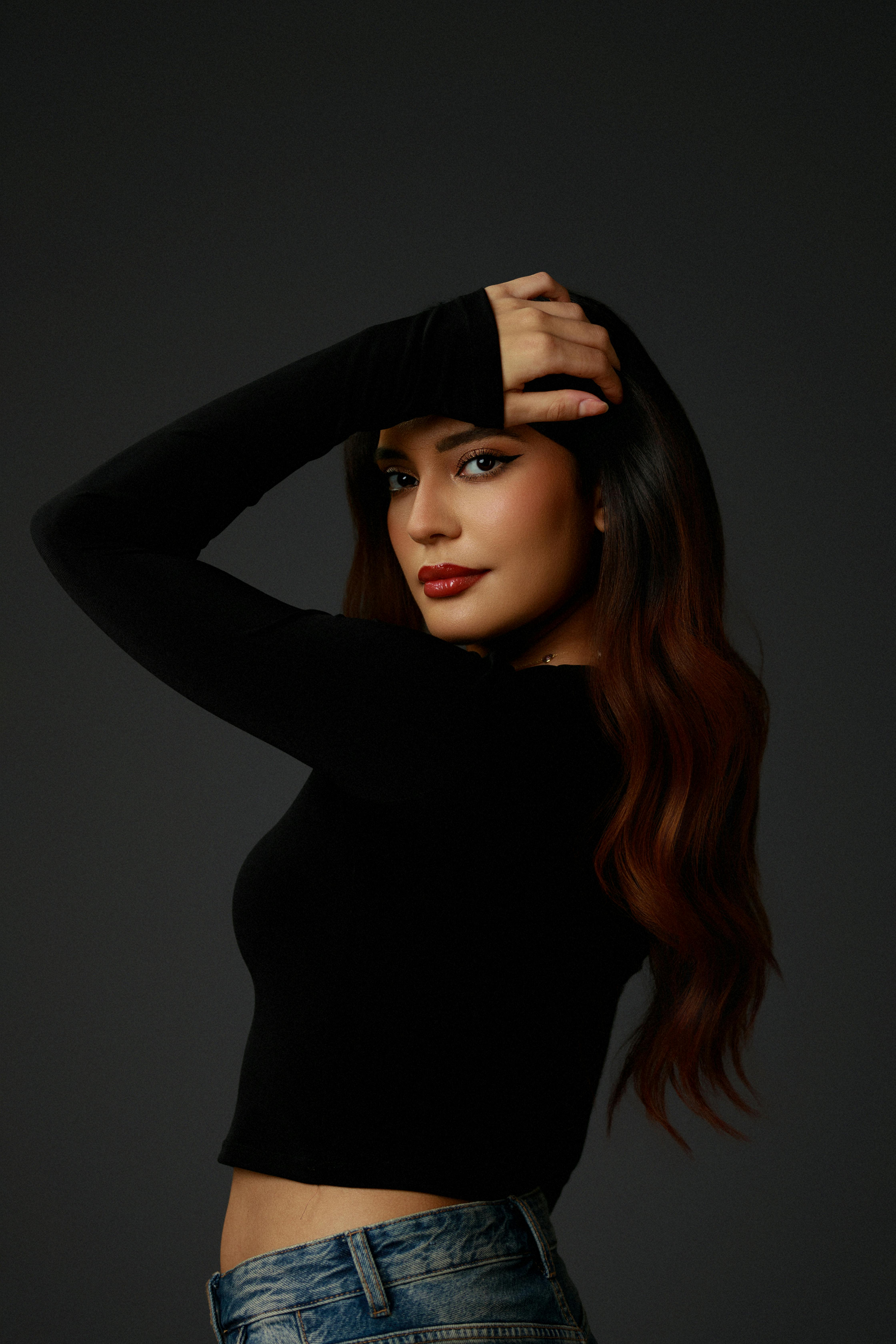 bezplatná Pozoruhodný portrét ženy s dlouhými vlasy, oblečené v černém topu a džínách, která sebevědomě pózuje. Základová fotografie