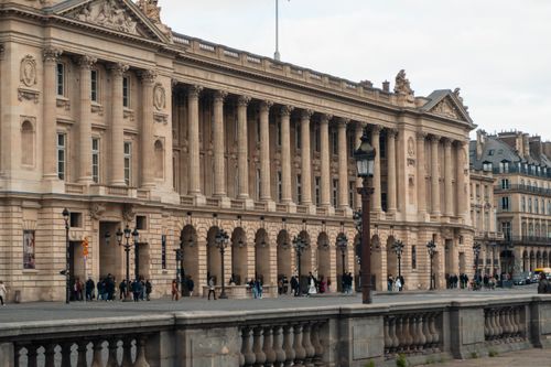 Free View of a neoclassical building facade in Paris with pedestrians walking below. Stock Photo
