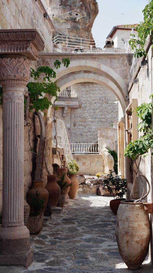 Free Charming stone alley with arches, pottery, and plants under a sunny sky, evoking a Mediterranean vibe. Stock Photo